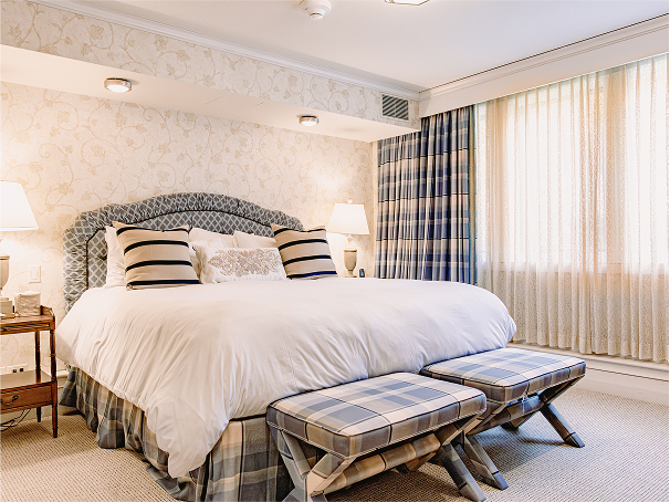 Cozy bedroom suite at RamsHorn Lodge featuring a plush king bed, decorative pillows, plaid ottomans, and elegant wallpaper, designed for a warm mountain retreat in Vail.